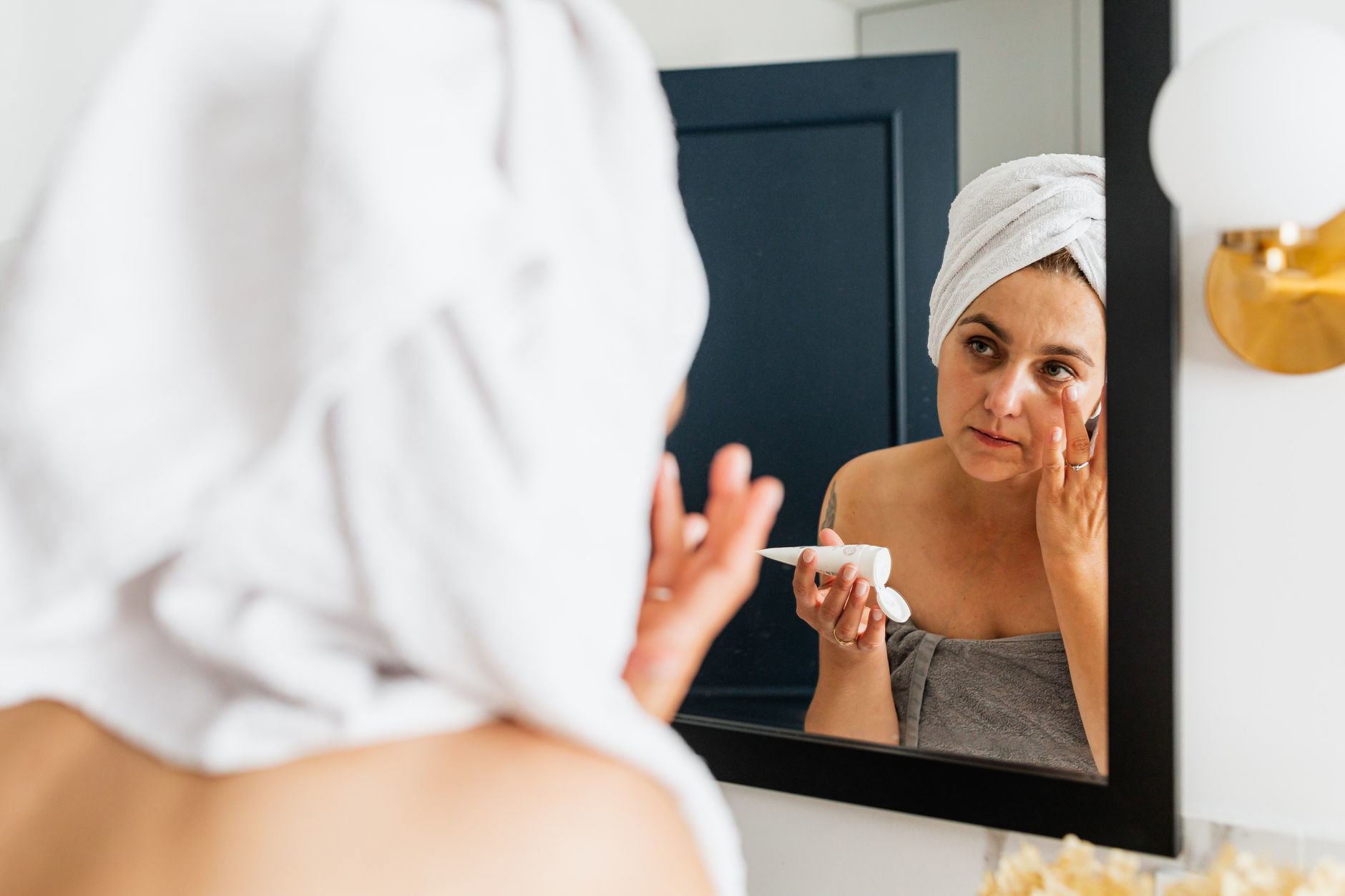 woman applying face sunscreen in bathroom mirror