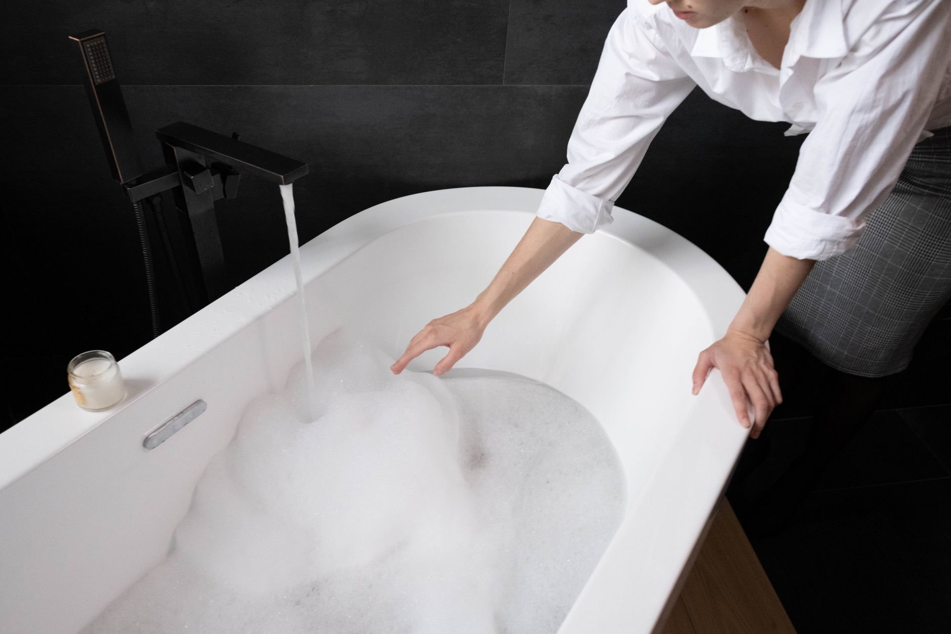 woman pouring bubble bath into running bath water