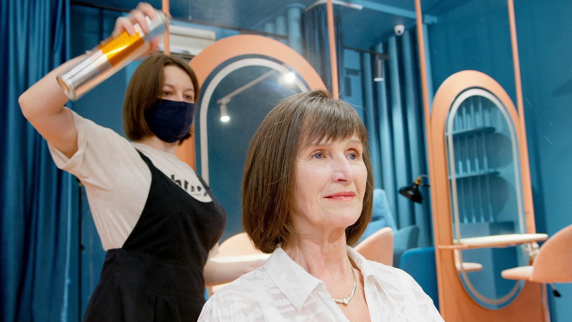 woman spraying hairspray on hair styling mirror