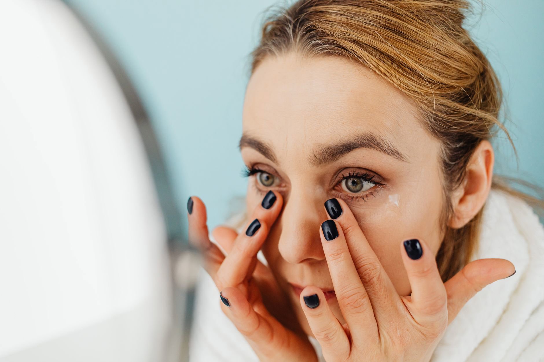 woman applying eye cream mirror