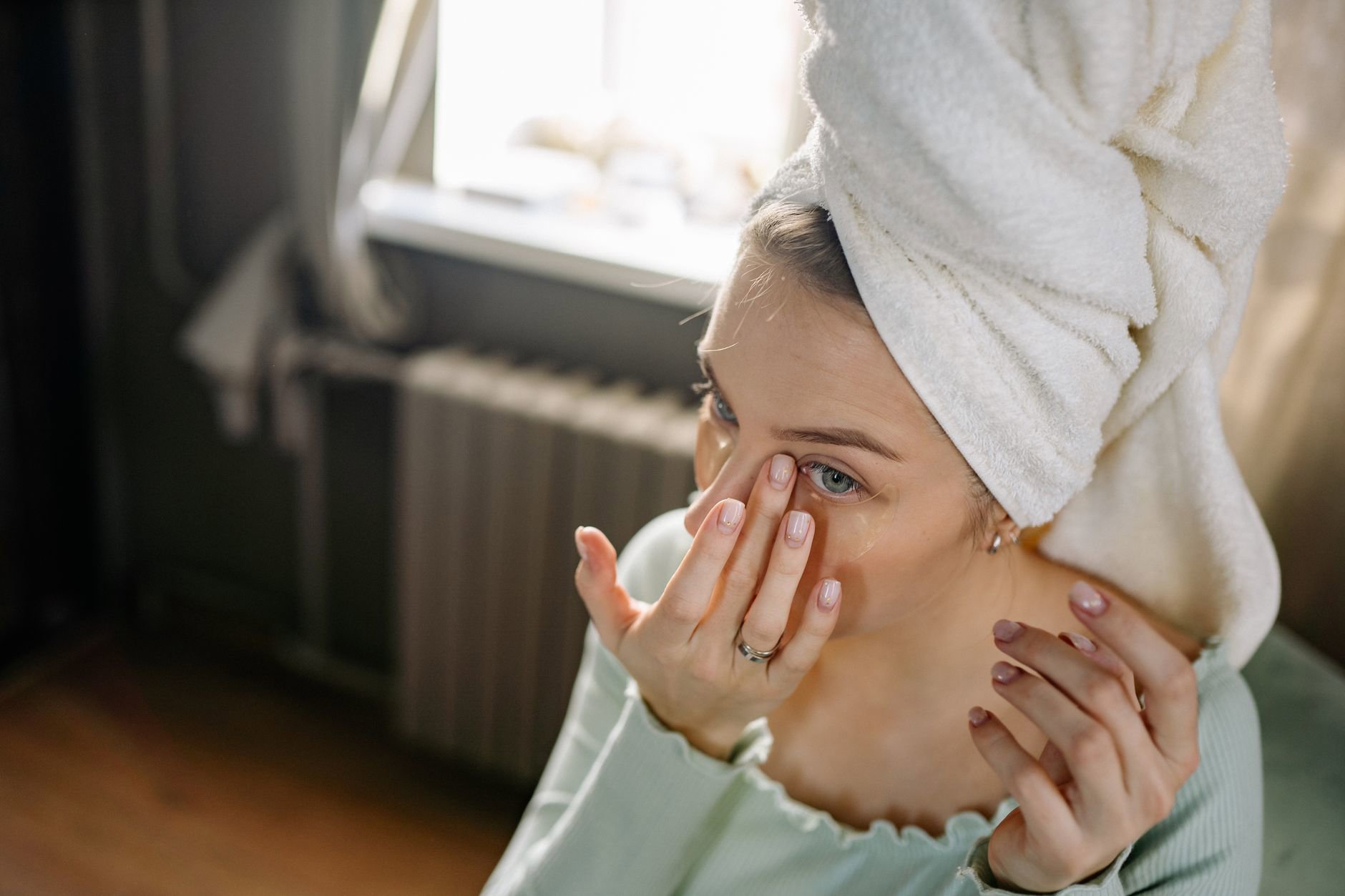 woman applying eye cream under eye in mirror