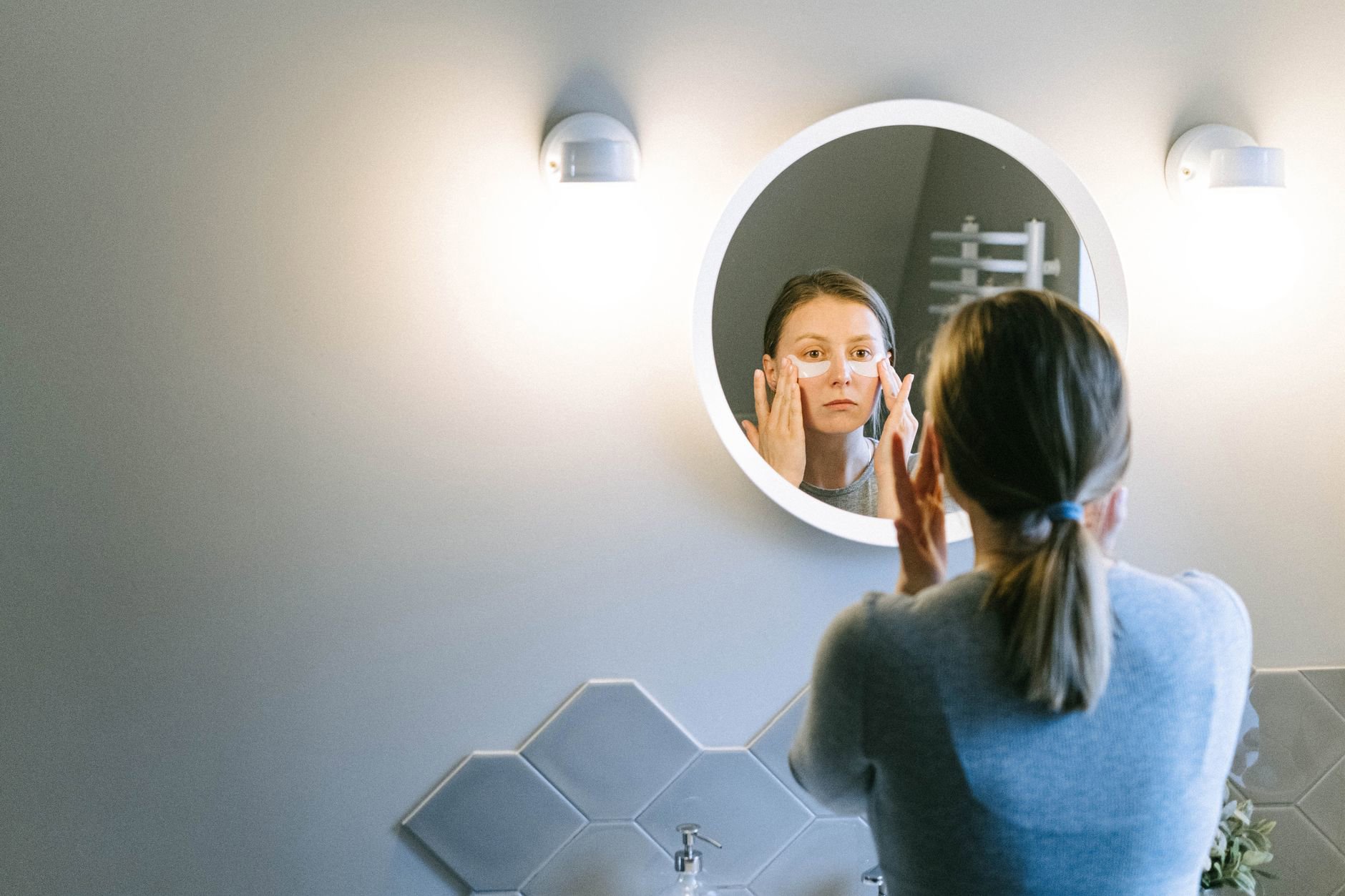 woman applying eye serum under eyes mirror