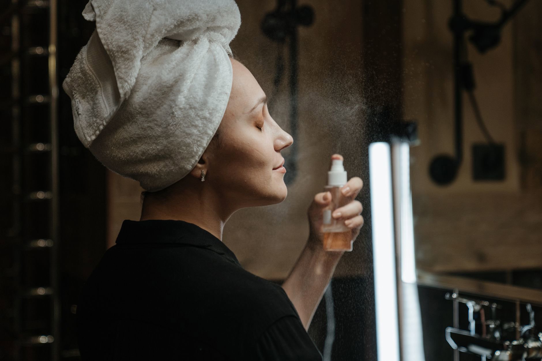 woman spraying face mist over makeup vanity