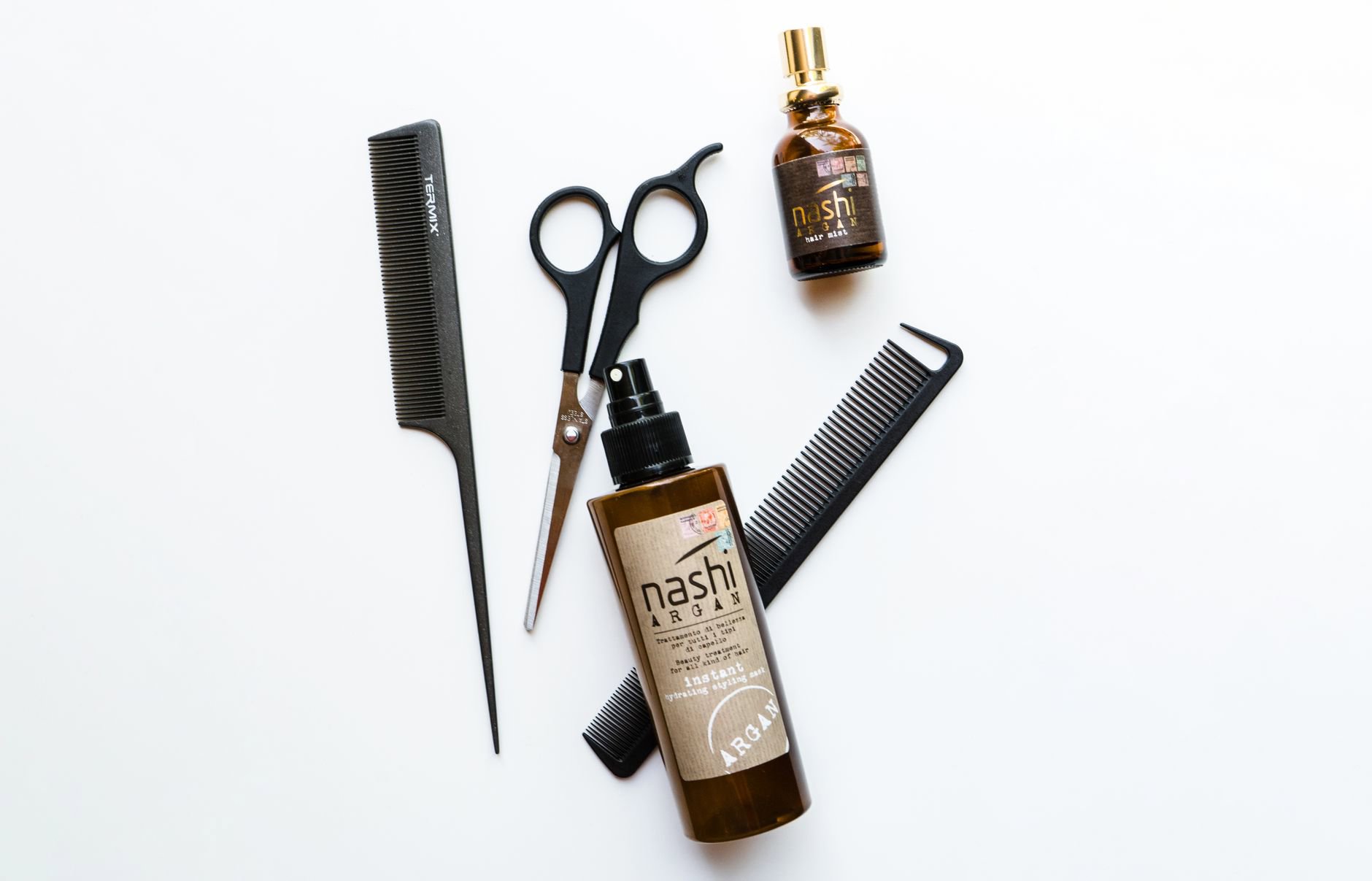 flatlay hair serums on white background with comb