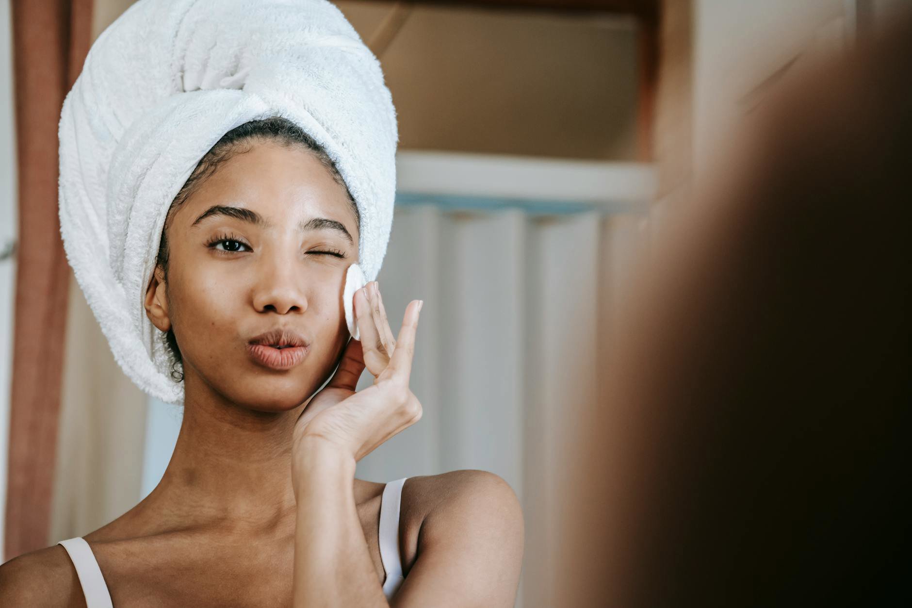 woman applying liquid exfoliant cotton pad bathroom mirror