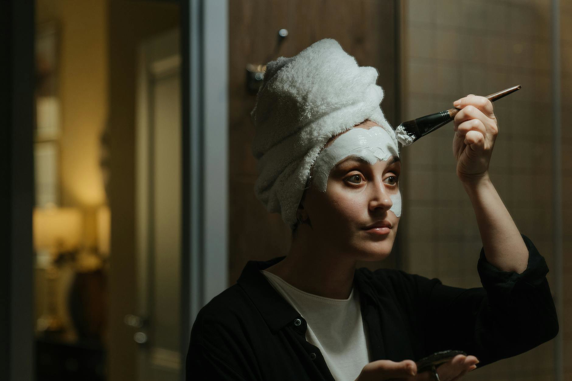 woman applying hair mask towel dried hair bathroom mirror