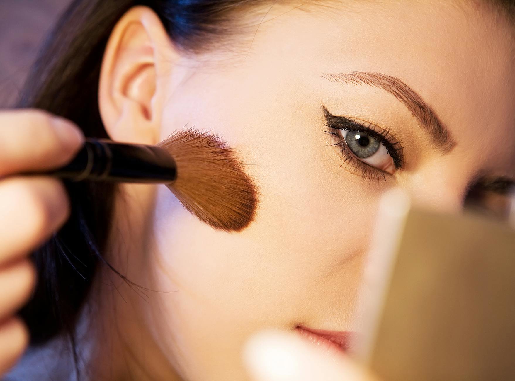 woman applying powder highlighter cheekbone close up