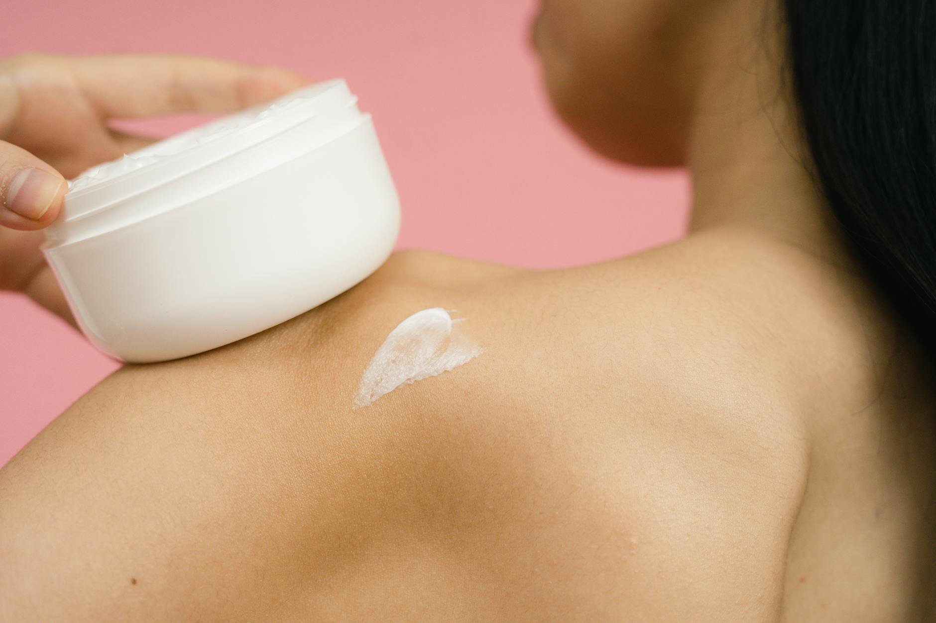 woman applying body cream on damp skin after shower