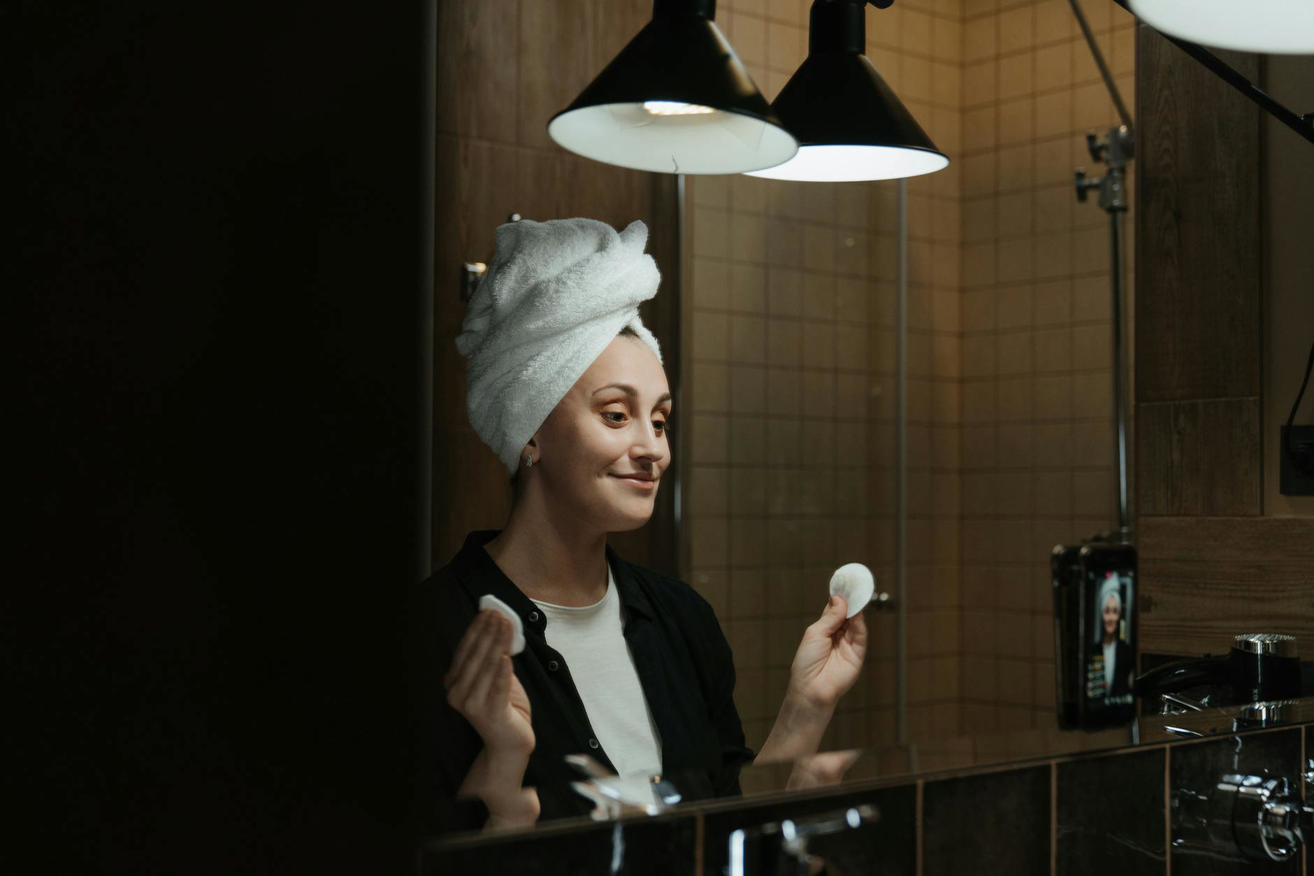 woman removing mascara cotton pad bathroom mirror