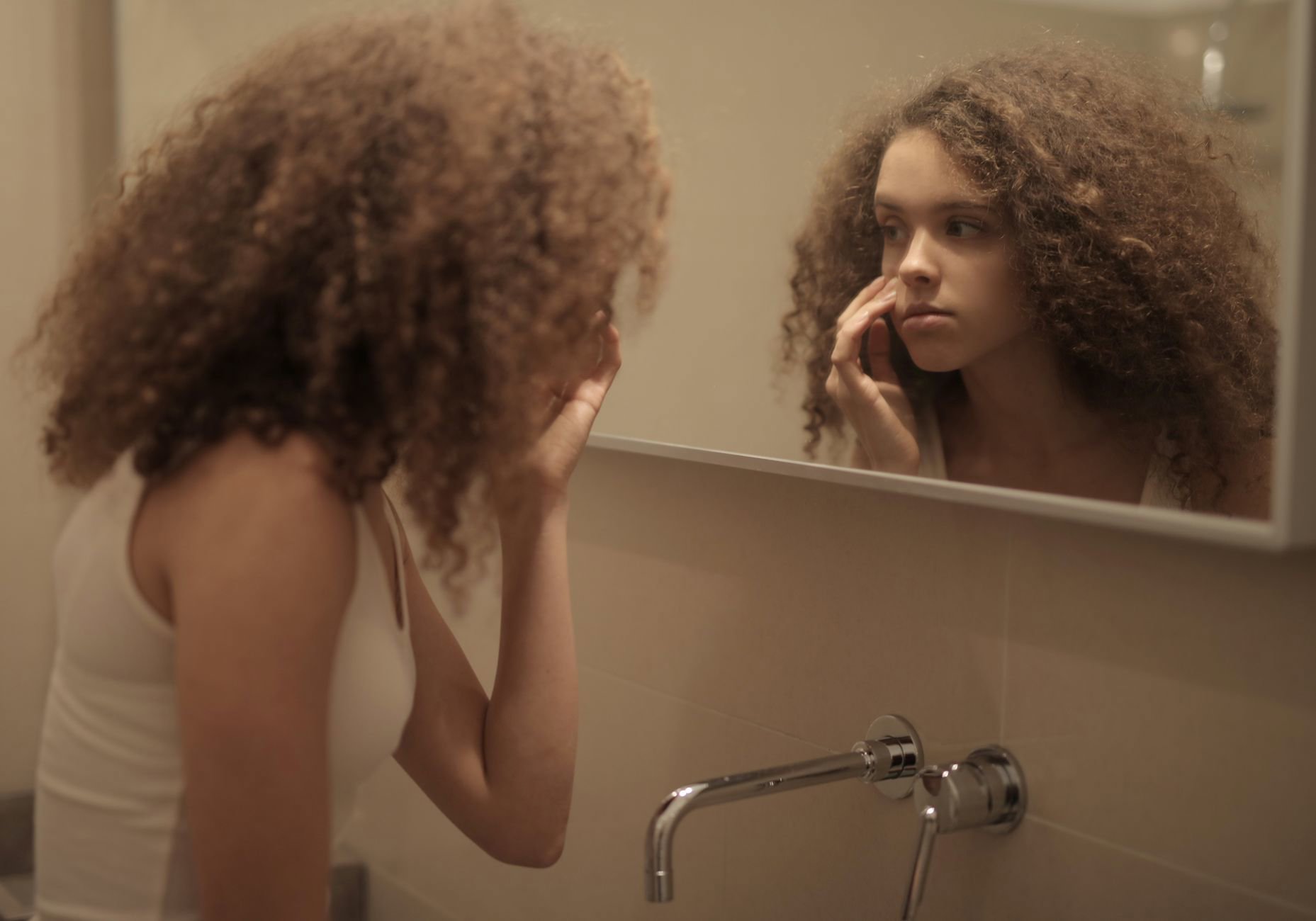 woman with wavy curly hair diffusing hair in bathroom mirror