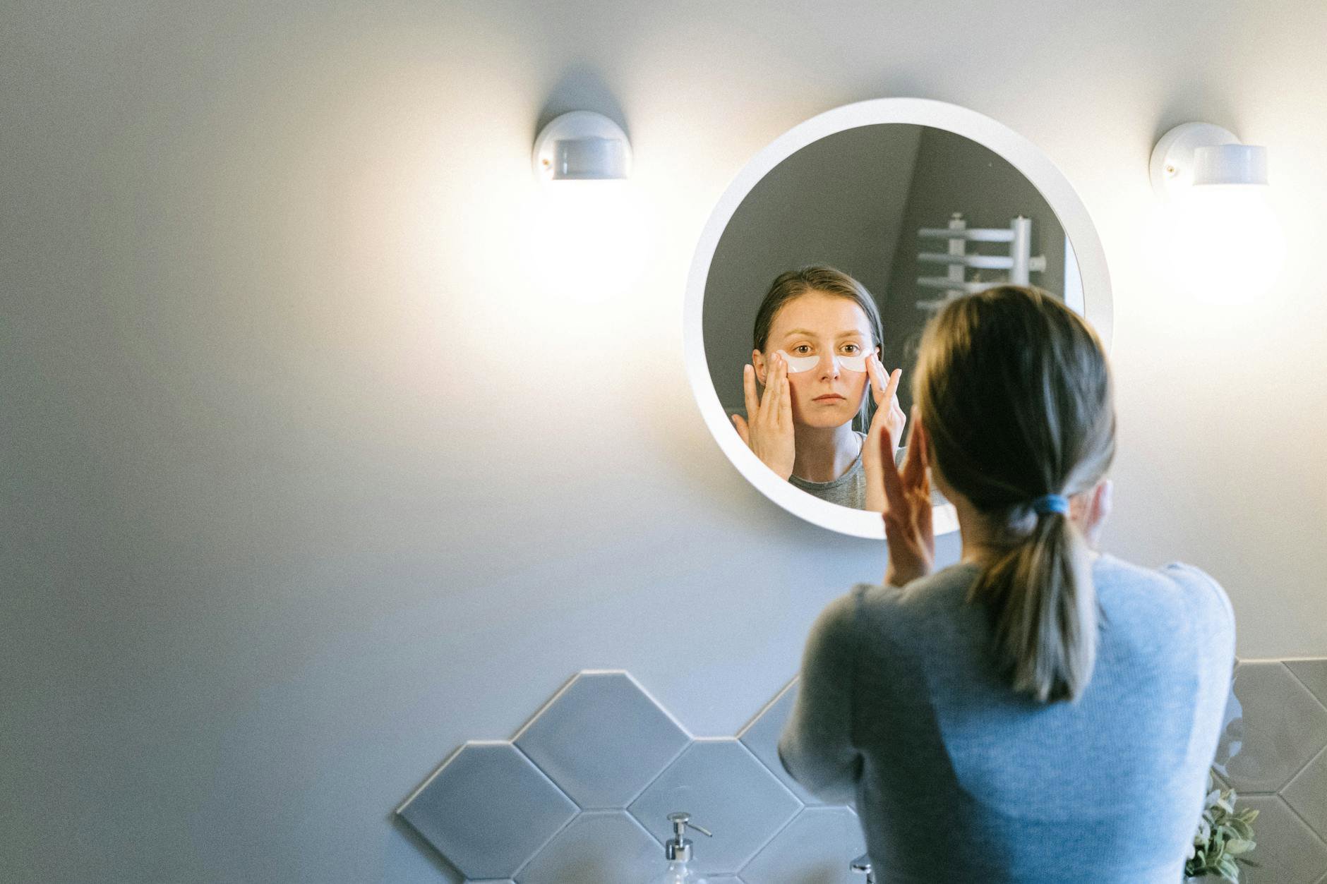 woman applying sunscreen under makeup mirror