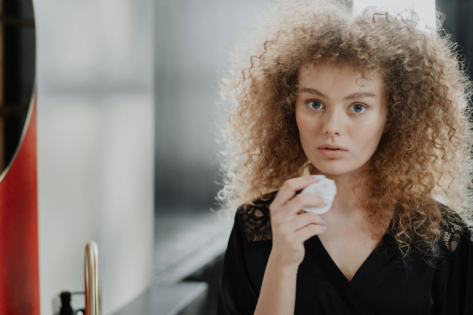 curly hair applying leave-in conditioner cream in bathroom mirror