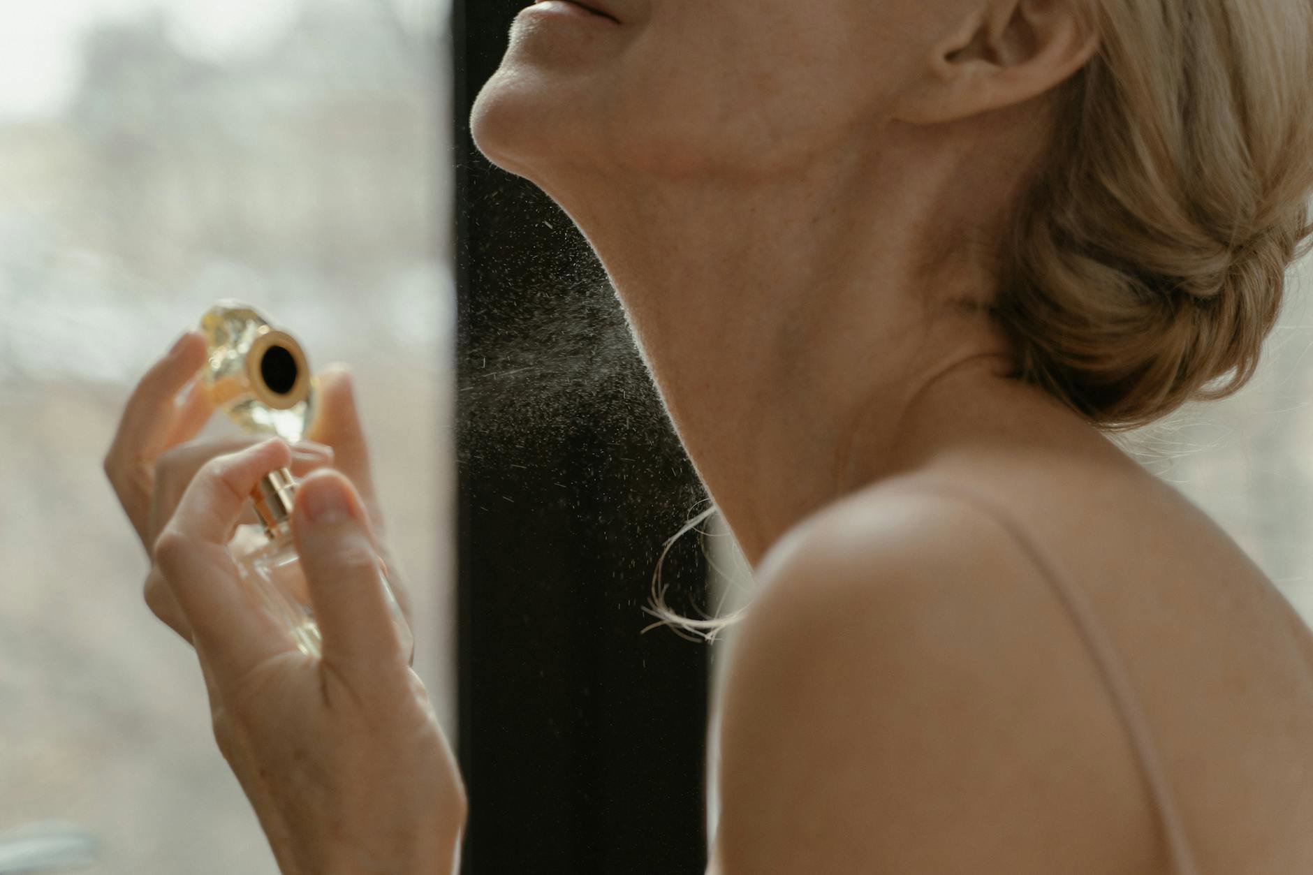 woman spraying perfume on neck close up