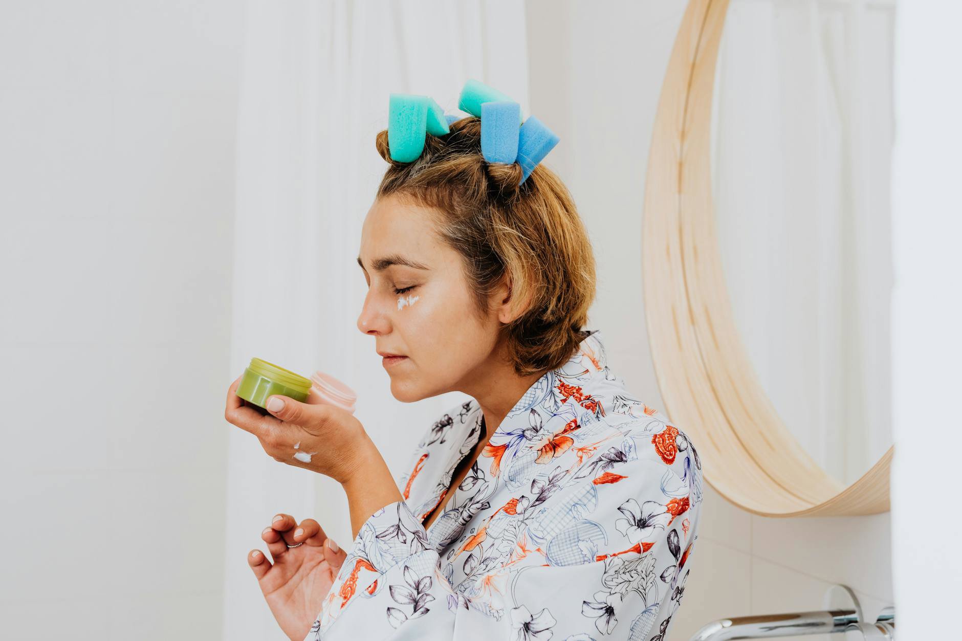 woman applying eye cream bathroom mirror