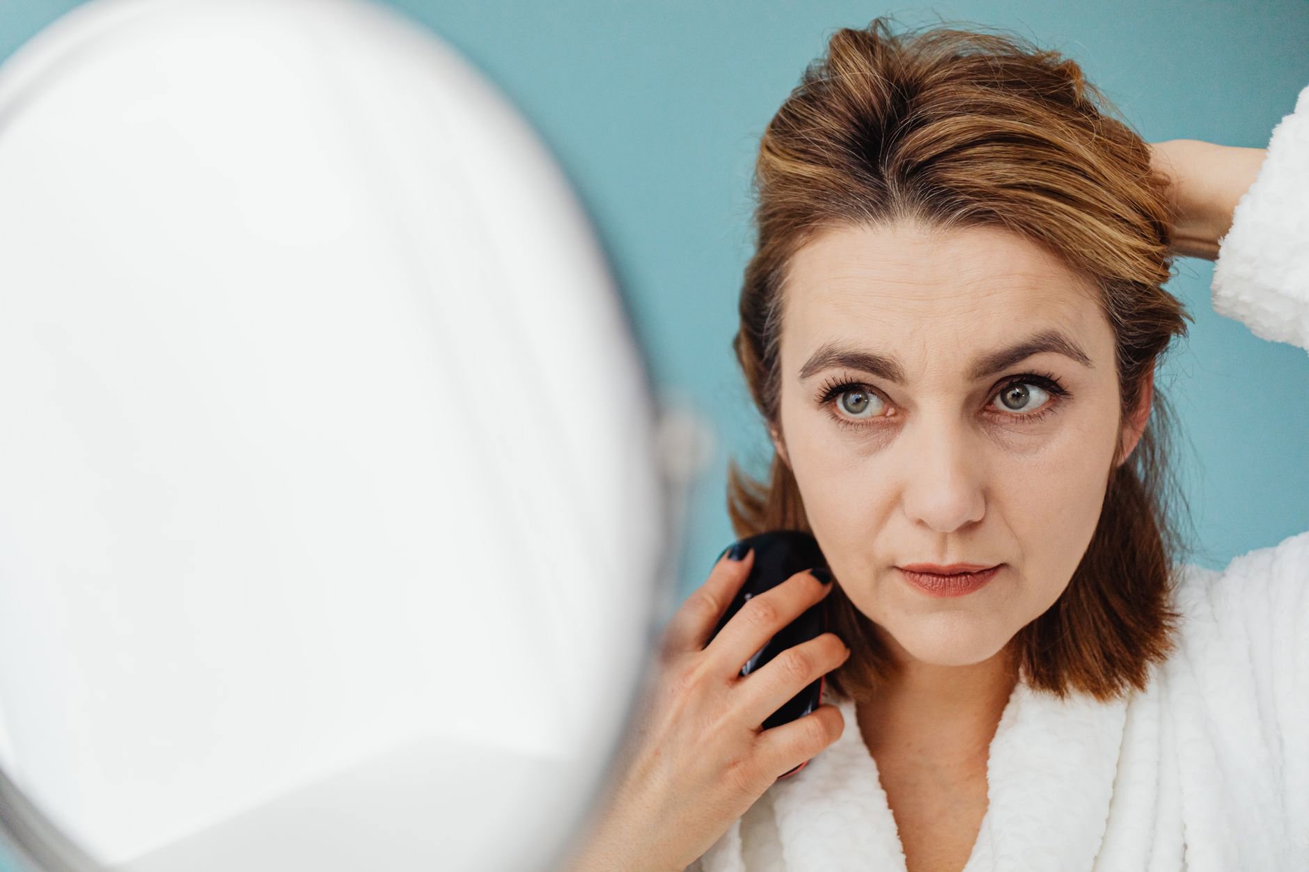 woman spraying water on hair strand bathroom mirror