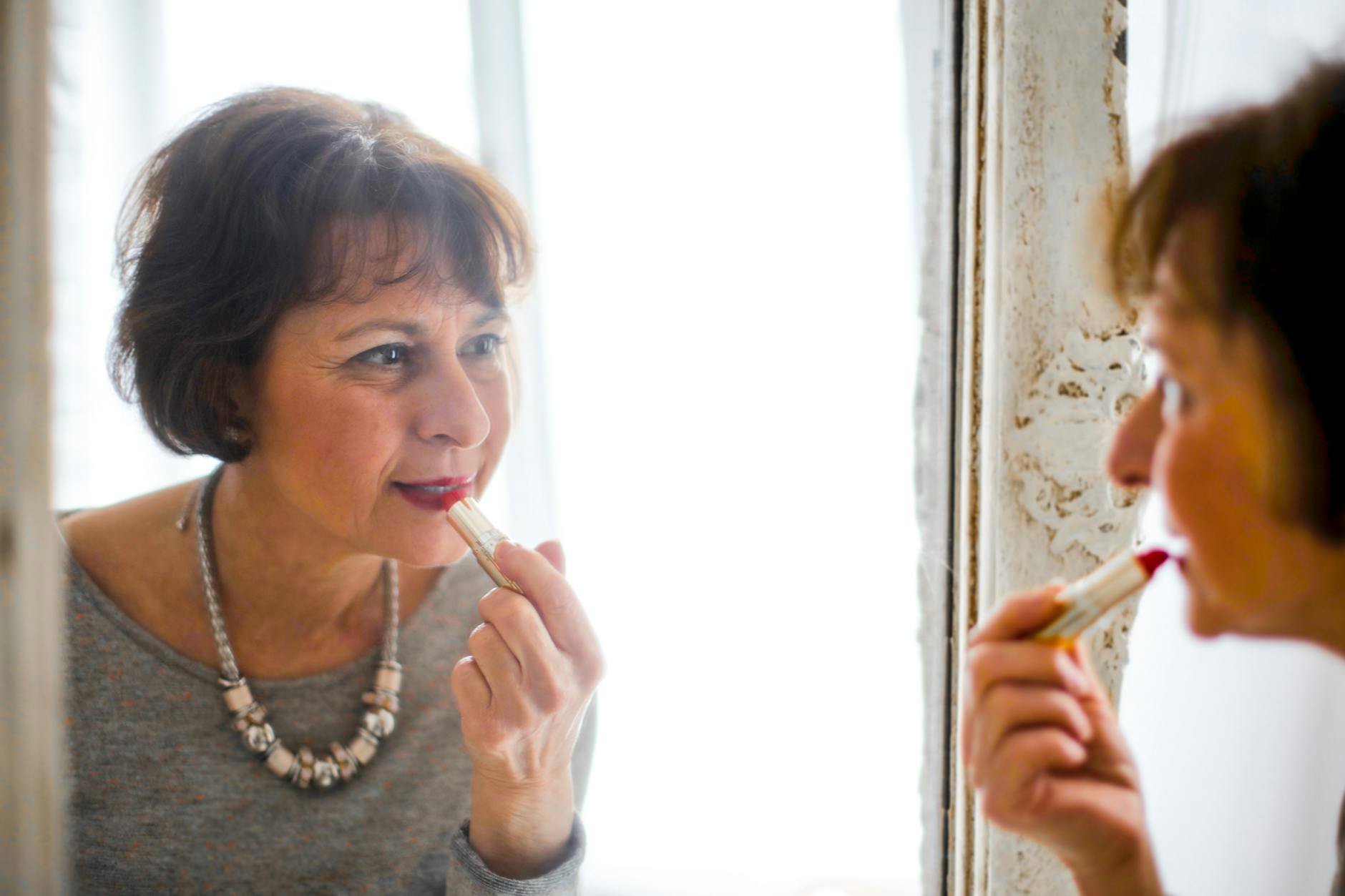 woman applying red lipstick in mirror