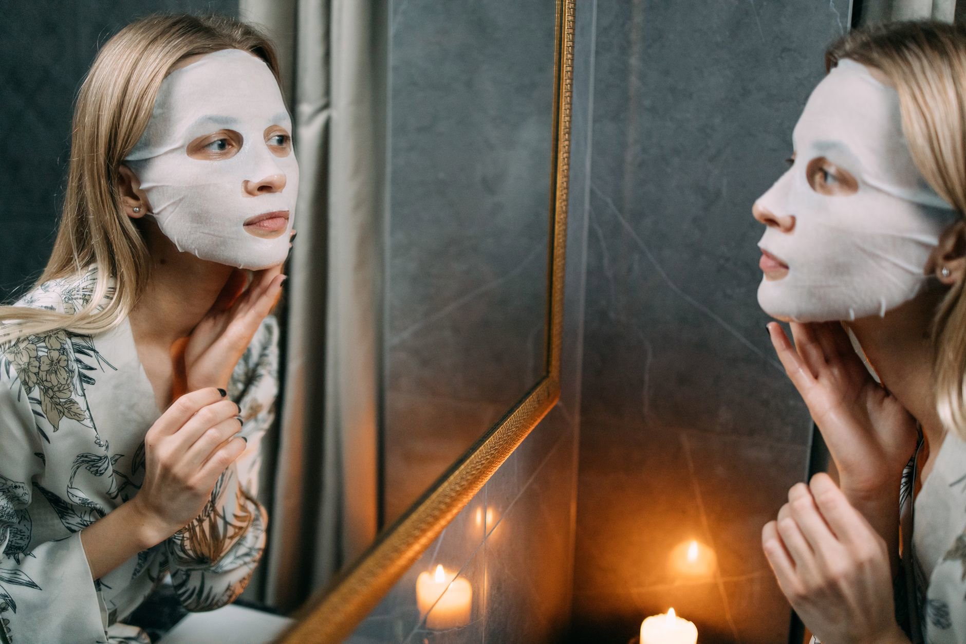 woman applying sheet mask bathroom mirror