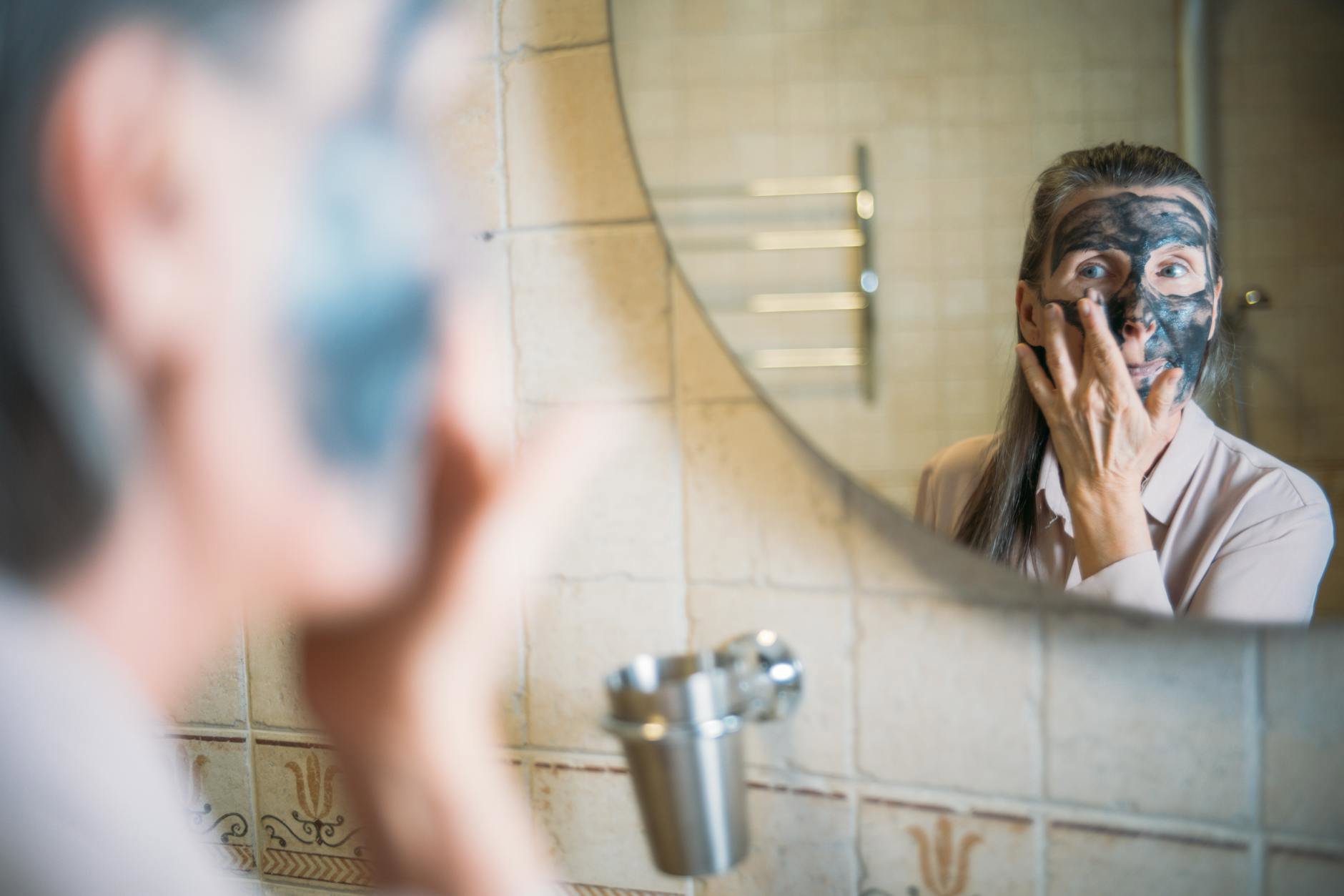 woman applying face moisturiser in bathroom mirror