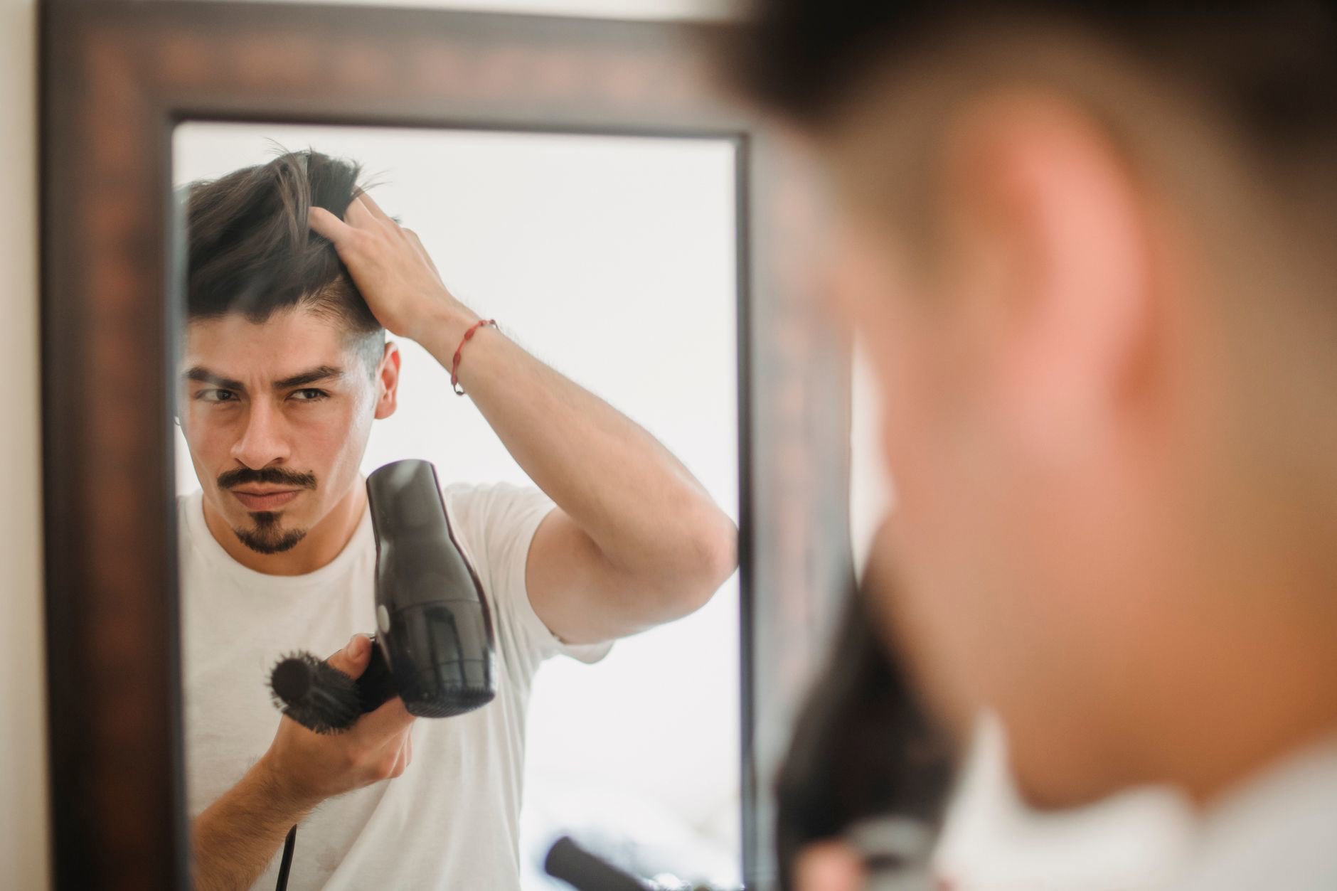 woman using hair dryer in bathroom mirror