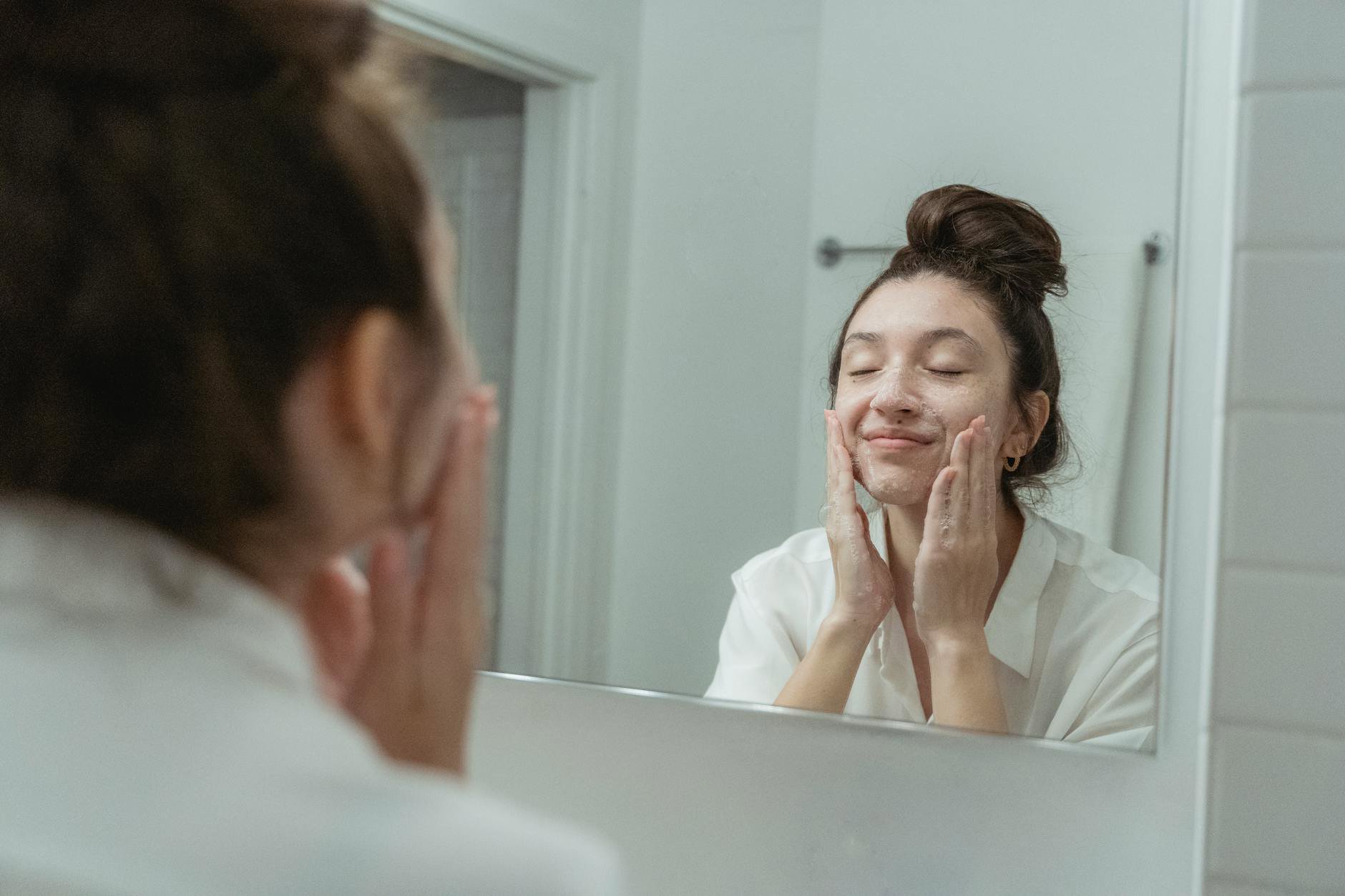 woman washing face with foam cleanser sink
