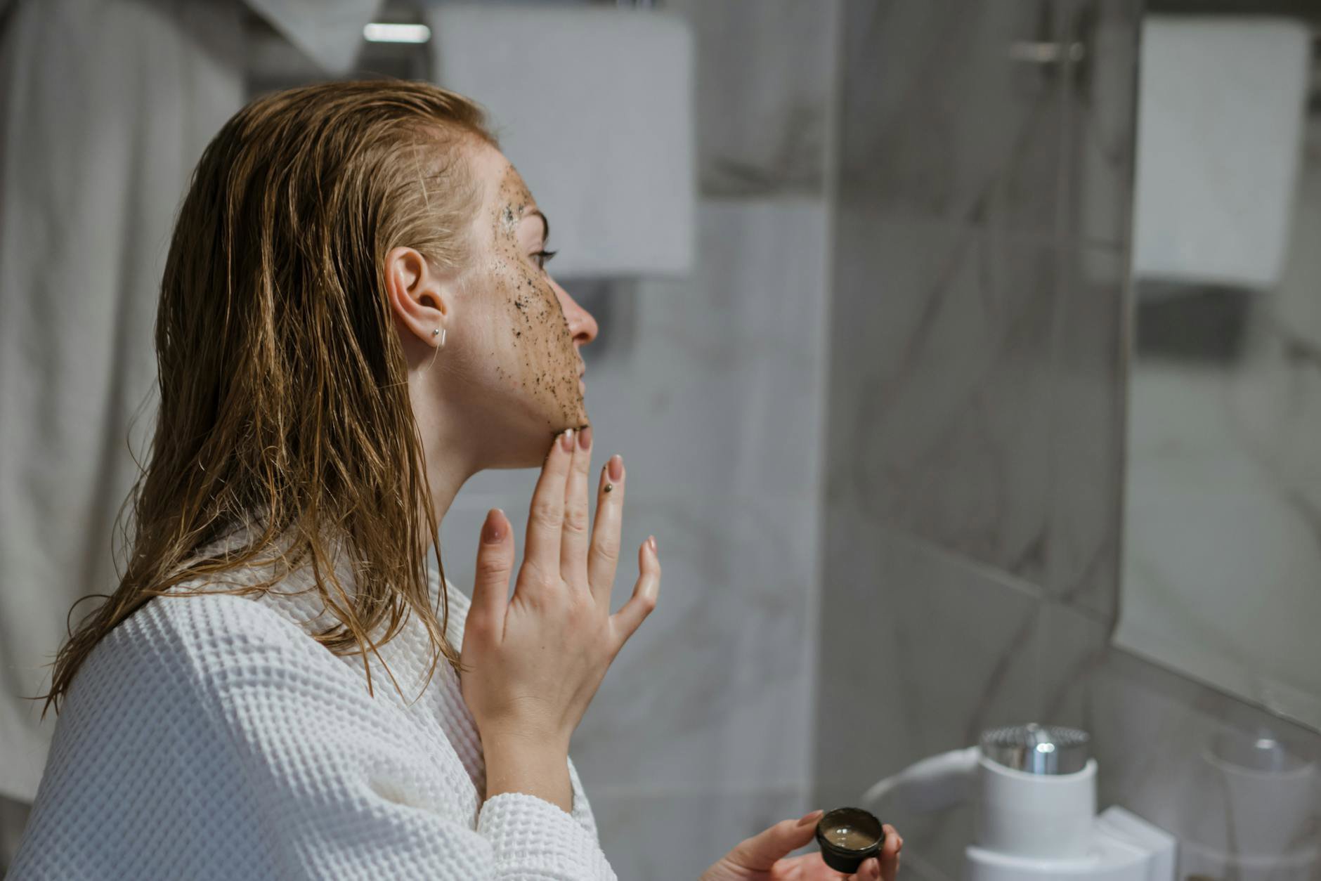 woman applying chemical exfoliant at night bathroom mirror