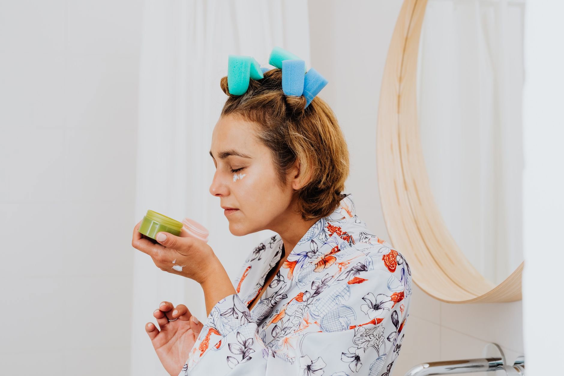 woman applying eye cream at bathroom mirror